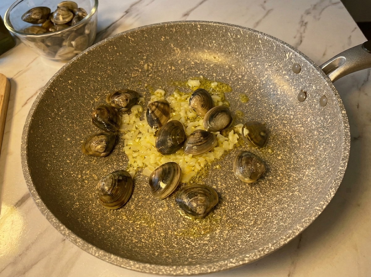 Vongole fresche chiuse aggiunte in una padella calda con aglio e cipolla soffritti.