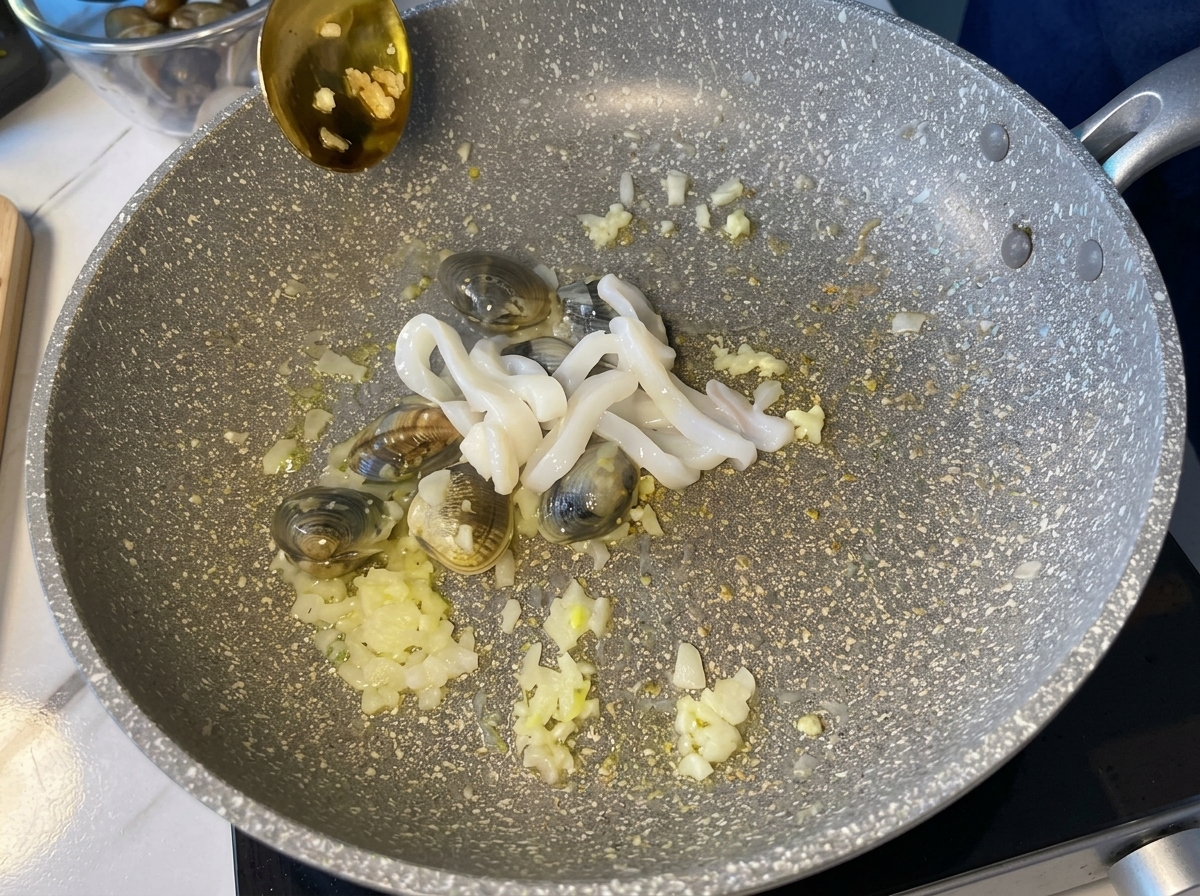 Anelli di calamaro crudo aggiunti a una padella calda contenente vongole e aromi.