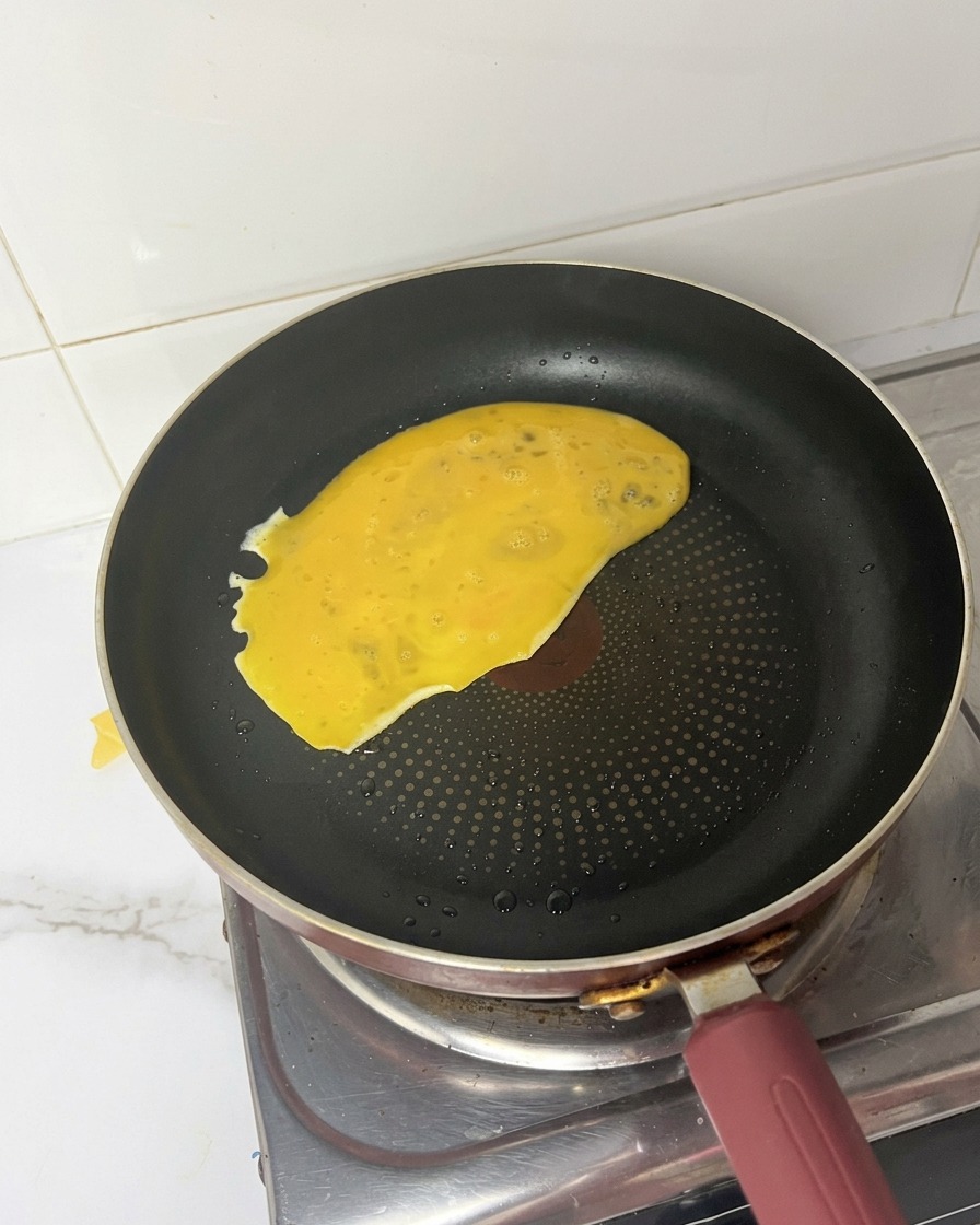 Composto di uova sbattute versato in una padella nera calda che si espande sulla superficie.