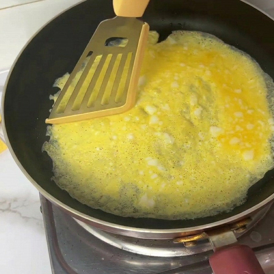 Una sottile frittata gialla tagliata in quattro parti con una spatola di metallo in una padella nera.