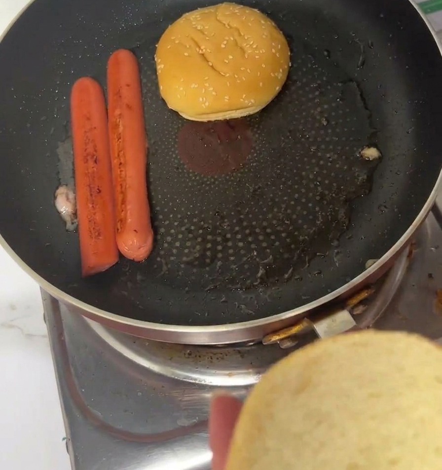 Panini al sesamo tostati dal lato del taglio in una padella accanto a würstel cotti.