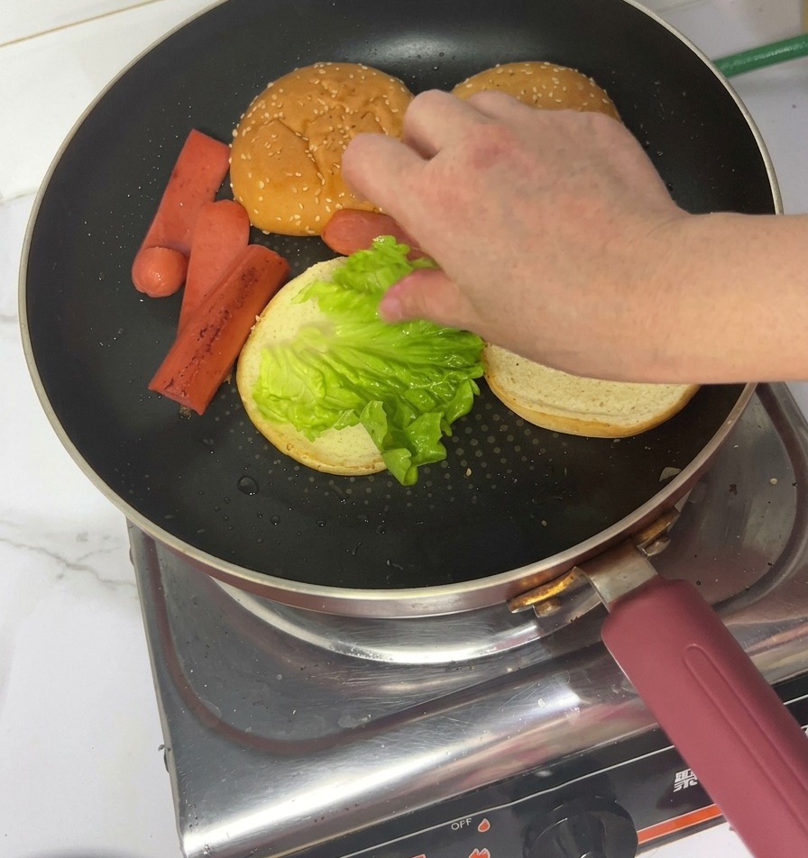 Una mano che mette una foglia di lattuga fresca su un panino tostato allinterno della padella.