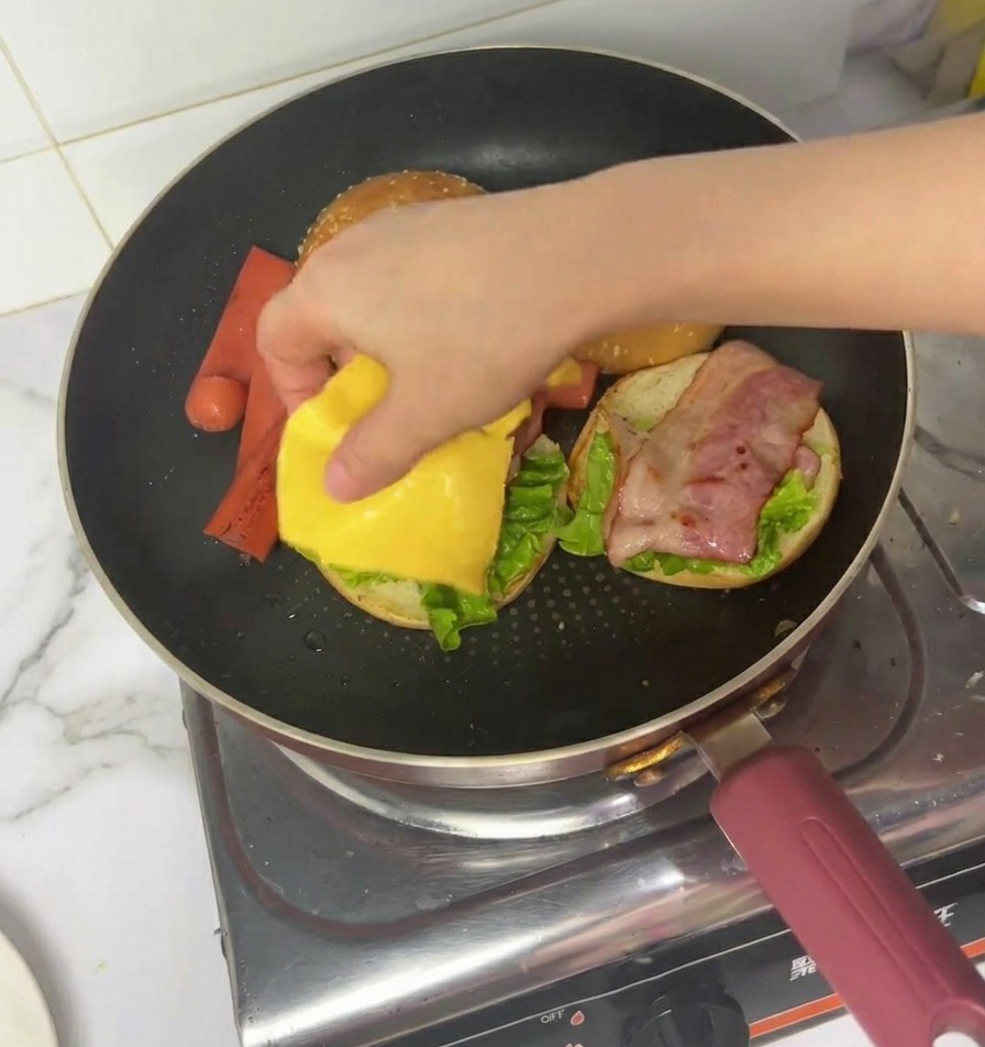 Una mano che mette una fetta di formaggio cheddar su un burger parzialmente assemblato in padella.