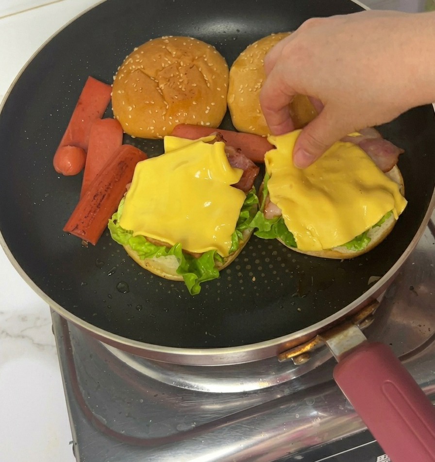 Mani che usano pinze per mettere fette di prosciutto cotto sullo strato di formaggio.