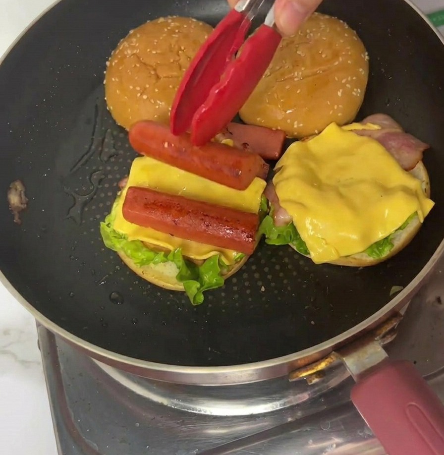 Un quarto di frittata sottile posizionato sul burger usando pinze rosse in padella.