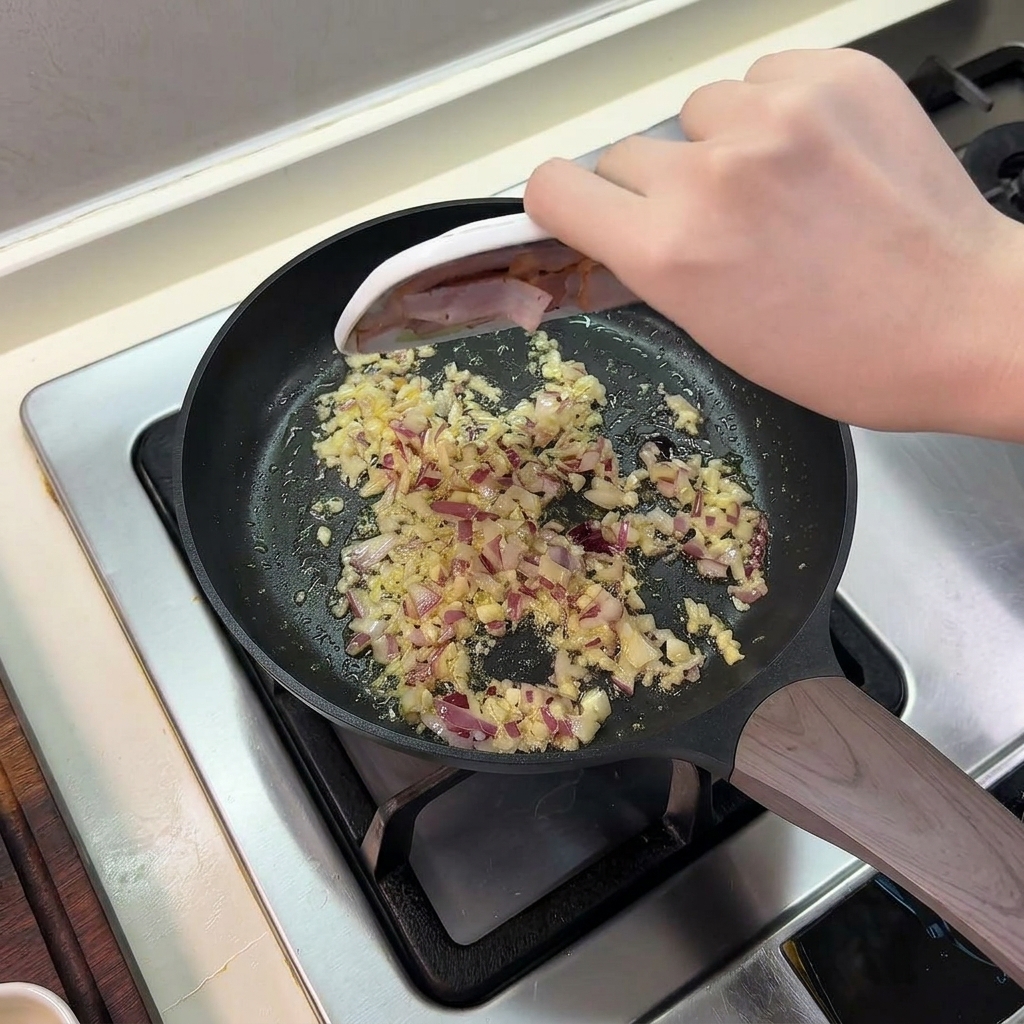 Pancetta a fette fatta scivolare da un piattino in una padella contenente cipolle e aglio soffritti.
