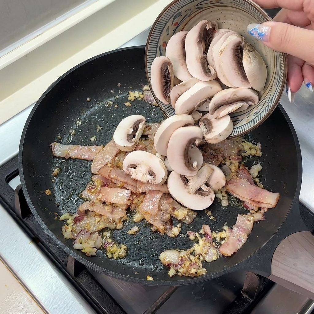 Funghi champignon freschi tagliati a fette versati da una ciotola di ceramica in una padella calda con pancetta, cipolle e aglio.