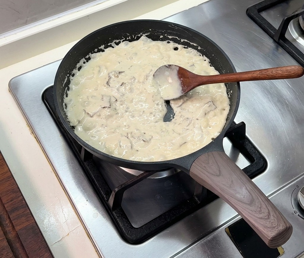 Una salsa cremosa e densa che sobbolle in una padella nera, mescolata con un cucchiaio di legno.