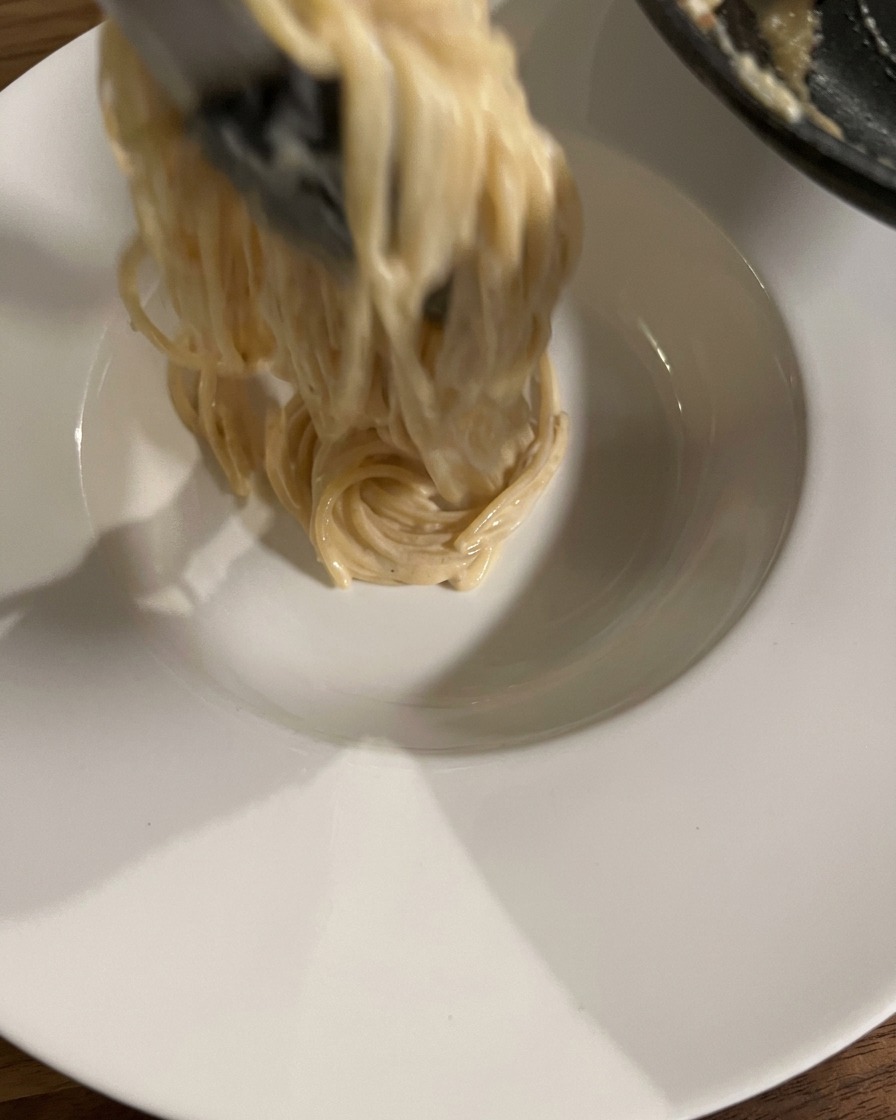 Pinze che arrotolano e sollevano una porzione di spaghetti cremosi in una ciotola bianca.