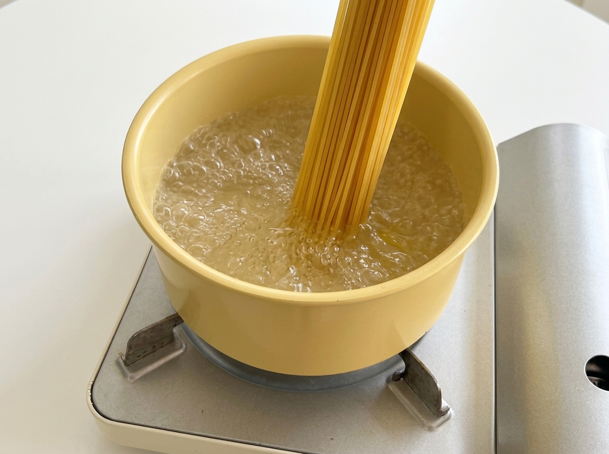 Spaghetti secchi immersi in una pentola gialla con acqua bollente.