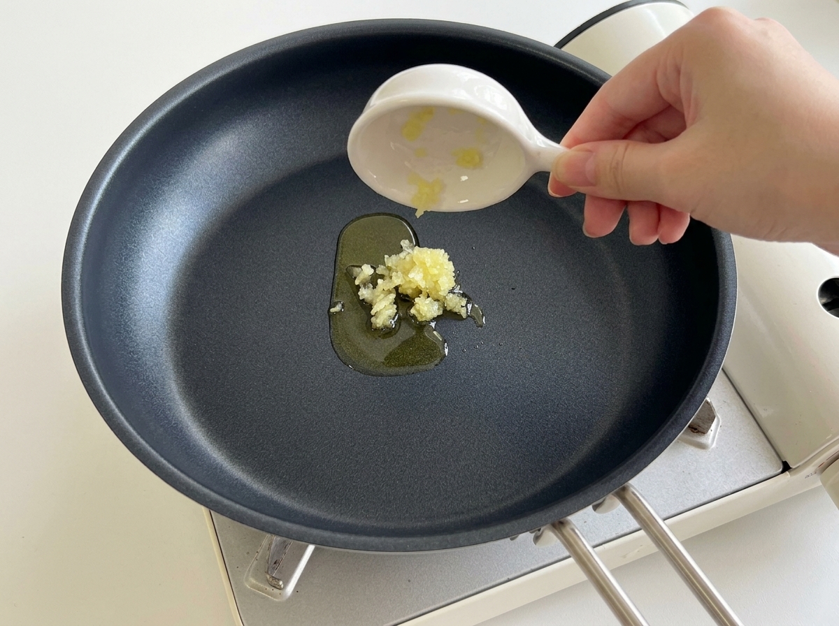 Aglio tritato versato da una ciotolina in una padella nera calda con olio.