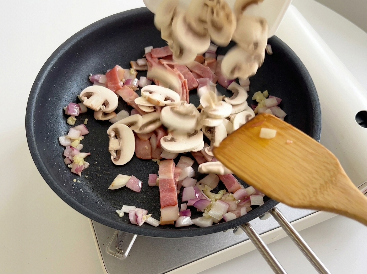 Funghi champignon affettati aggiunti in padella con pancetta e cipolle.