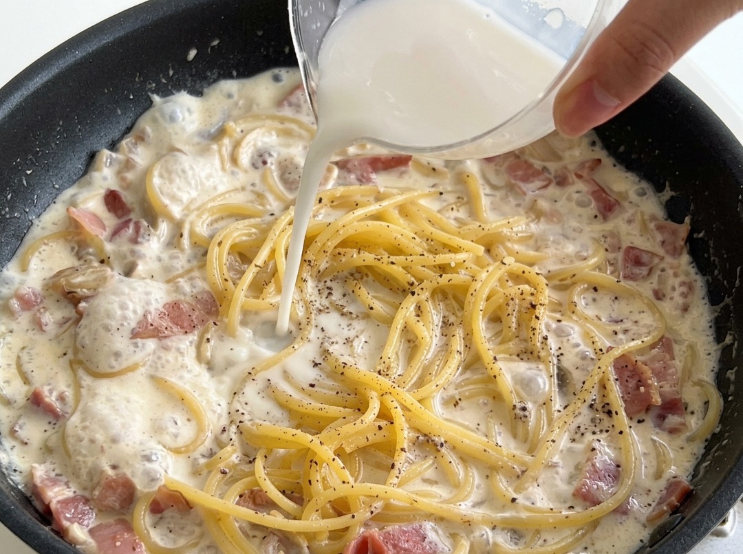 Versamento di una miscela di amido e acqua su spaghetti in padella con crema di latte.
