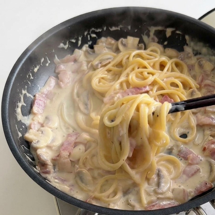 Bacchette che girano spaghetti cremosi in padella con salsa al latte bollente, pancetta e funghi.