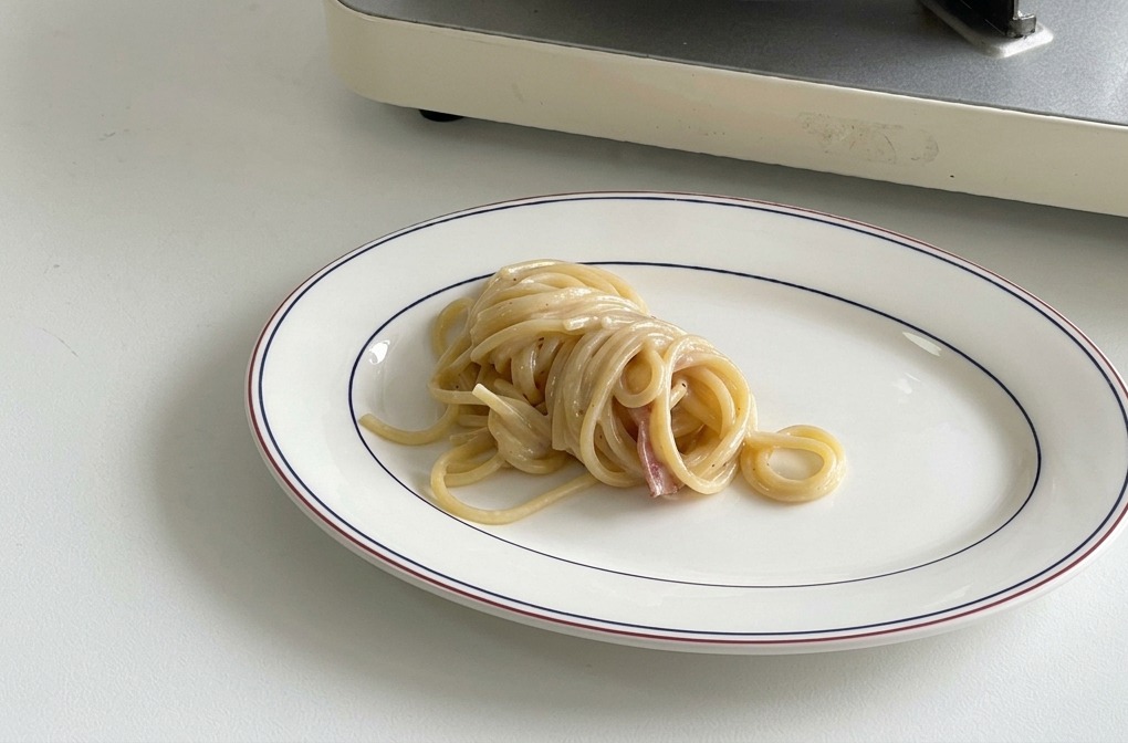 Un nido di spaghetti cremosi al centro di un piatto ovale bianco con bordo decorato.