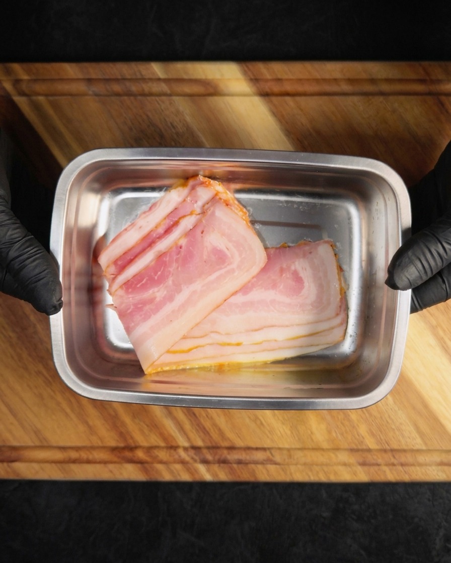 Fette di pancetta cruda disposte in un vassoio metallico rettangolare.