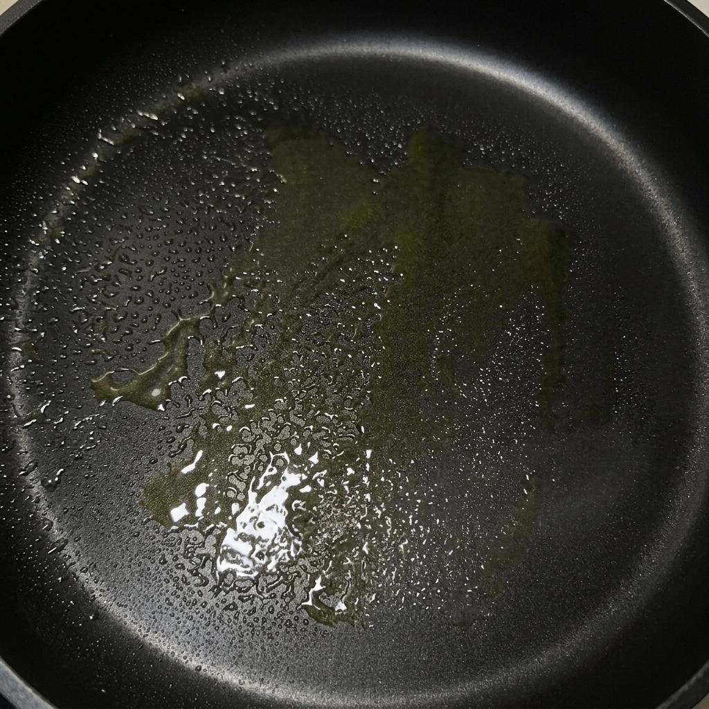 Una padella nera con un velo di burro fuso e olio doliva pronta per la cottura.
