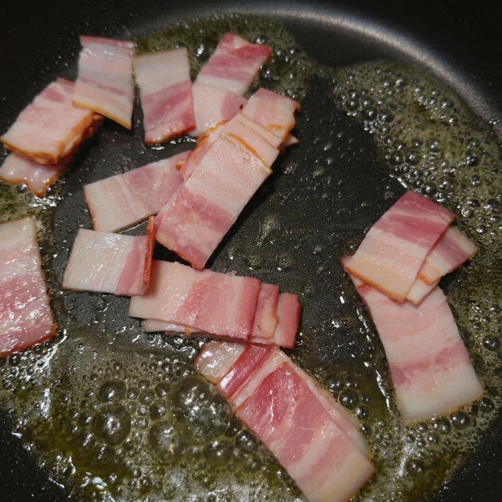 Striscioline di pancetta che sfrigolano e dorano in una padella nera.