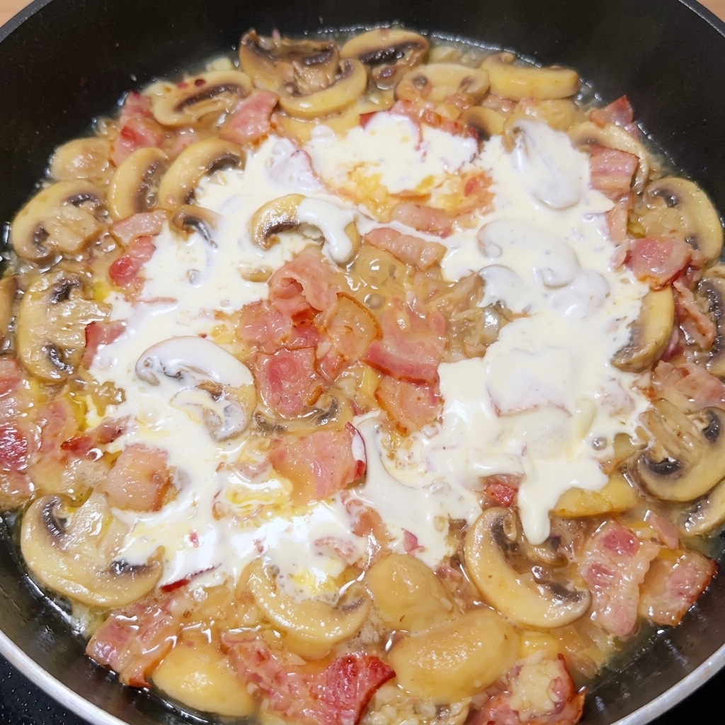 Panna liquida versata in padella con il condimento di pancetta e funghi.
