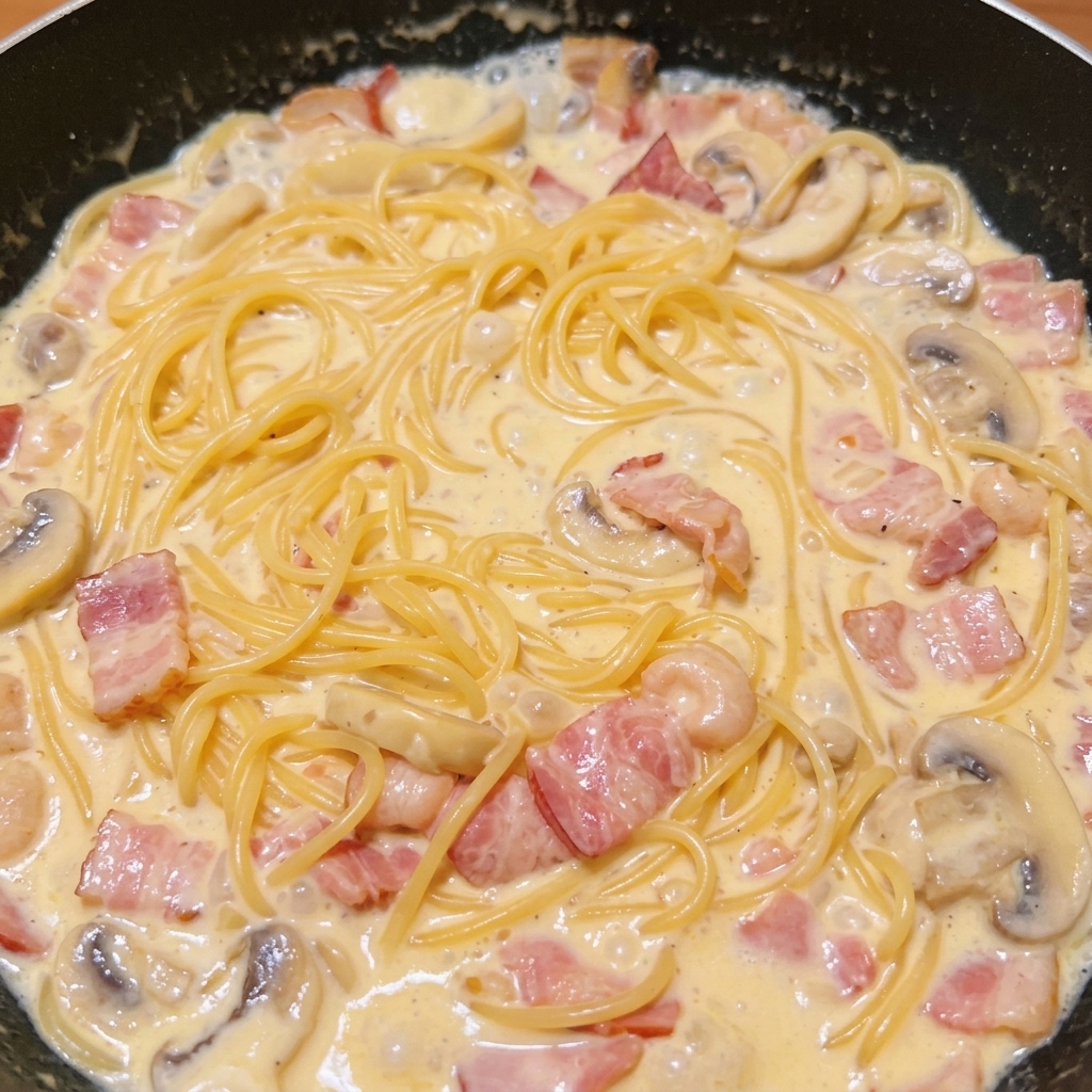 Spaghetti mescolati alla ricca salsa cremosa con pancetta e funghi in una padella scura.