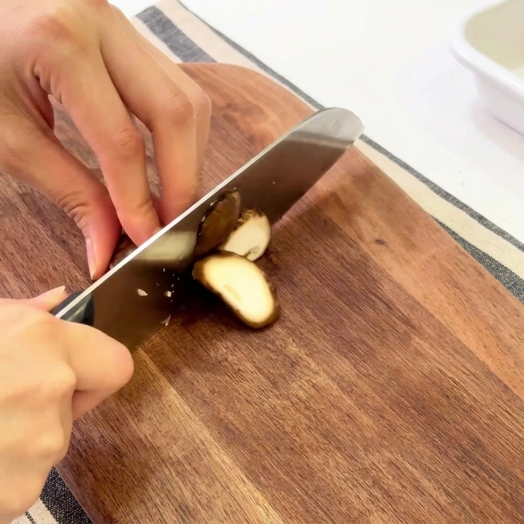 Mani che affettano funghi shiitake freschi su un tagliere di legno.