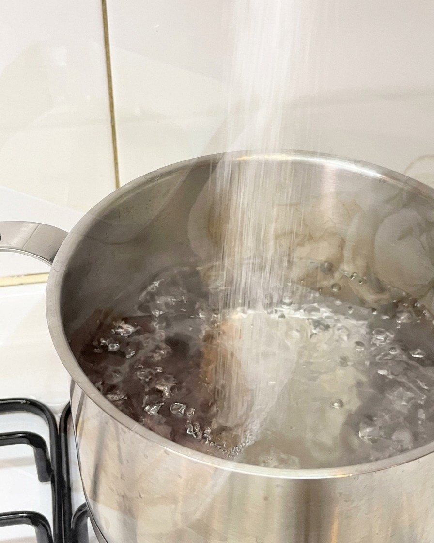 Sale versato in una pentola dacciaio con acqua in piena ebollizione.