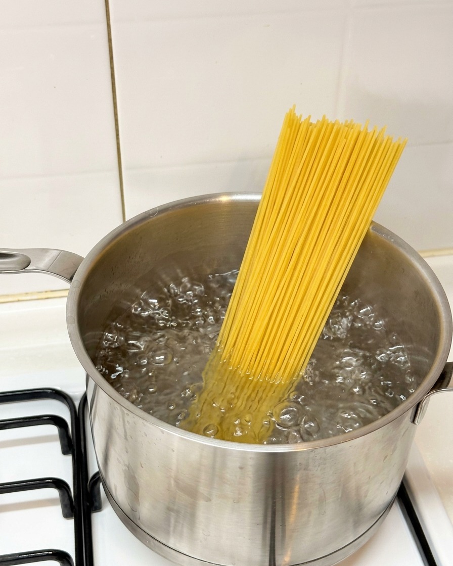 Spaghetti secchi messi in una pentola di acqua bollente sul fornello.