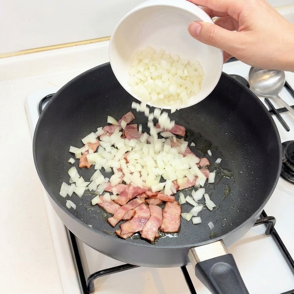 Una mano che versa cipolla bianca tritata da una ciotola in una padella con la pancetta rosolata.