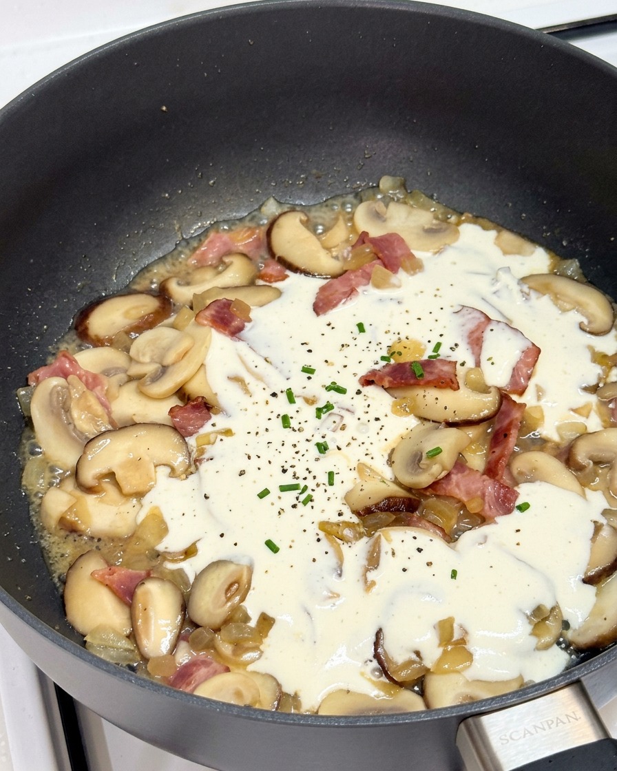 Panna da cucina che sobbolle in padella con funghi e pancetta.