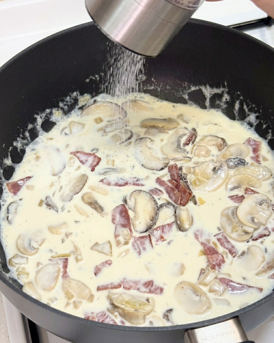 Una persona che usa un macinapepe per aggiungere pepe nero fresco in una padella con salsa cremosa.