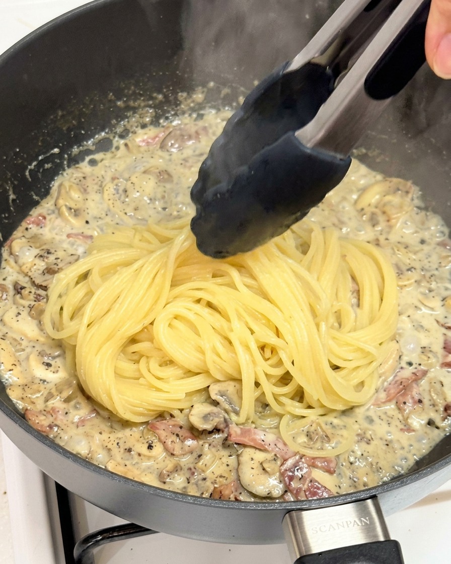 Pinze che trasferiscono spaghetti appena bolliti in una padella con salsa al tartufo.