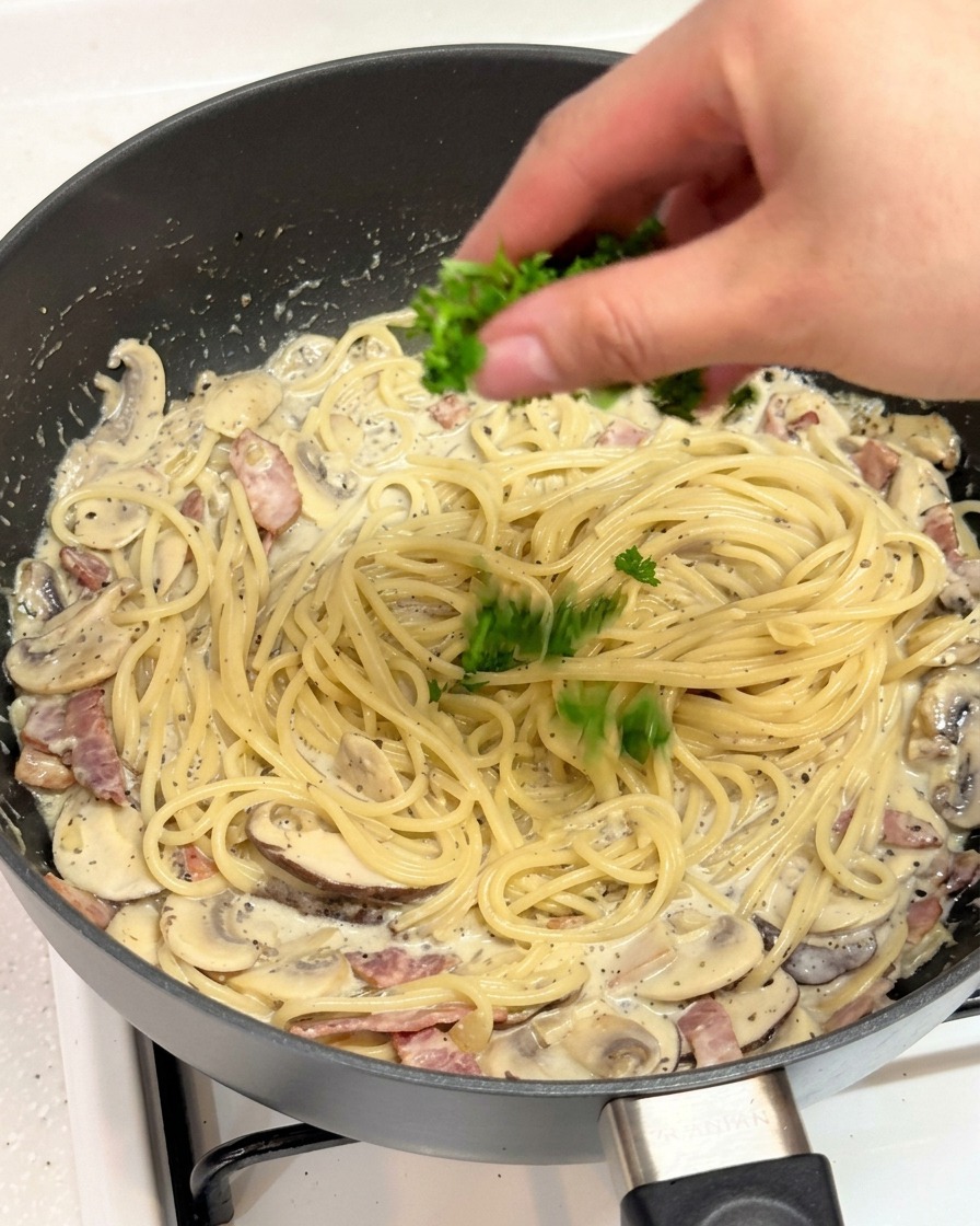 Una mano che cosparge prezzemolo verde tritato su una padella di pasta cremosa.