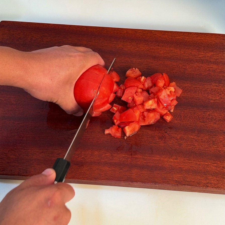 Una mano che usa un coltello da chef per tagliare un pomodoro rosso pelato su un tagliere di legno scuro.