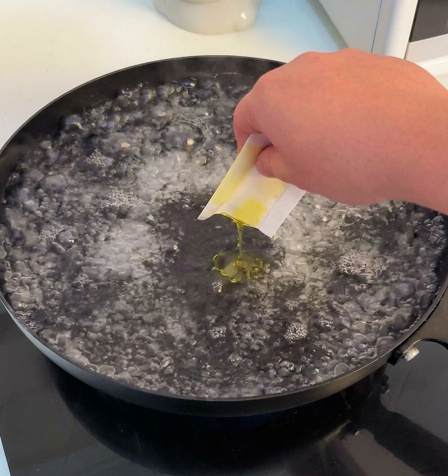 Una mano che versa sale e olio doliva in una pentola larga con acqua che bolle vigorosamente.