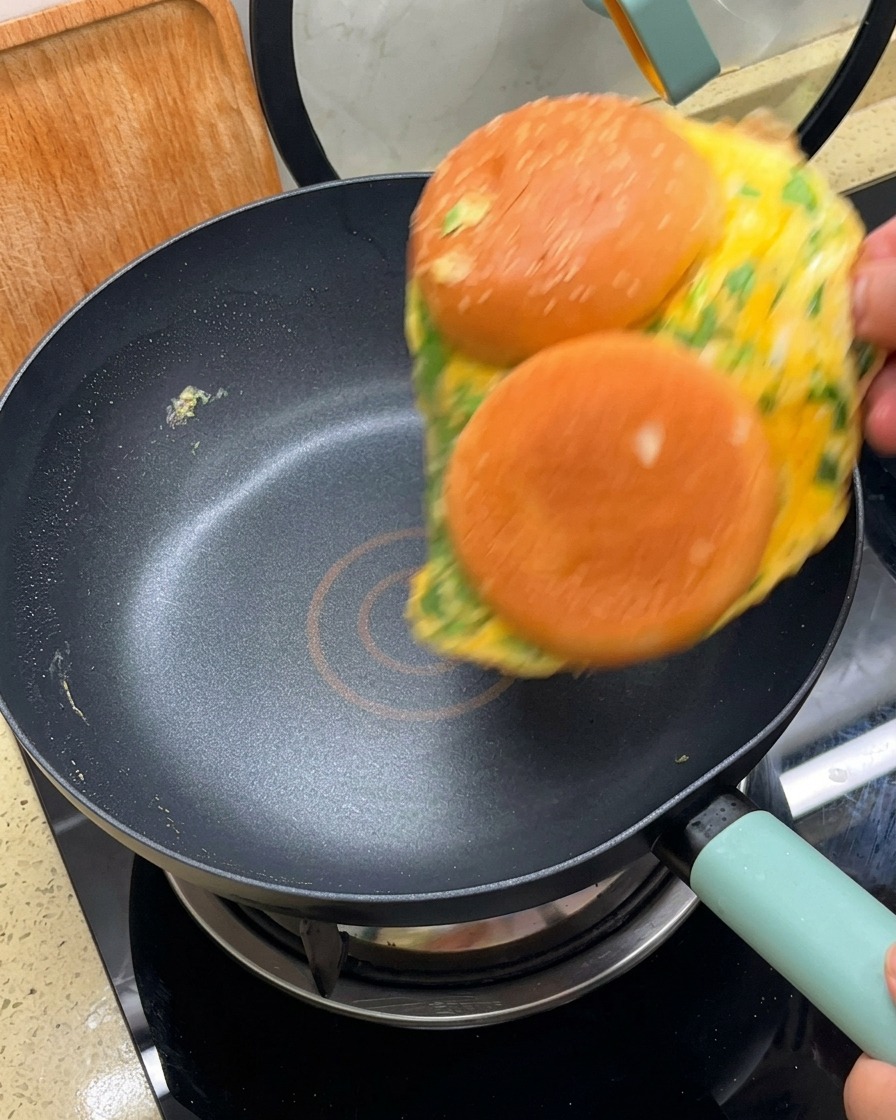 Unomelette con le due metà del pane attaccate che viene girata in una padella antiaderente nera.
