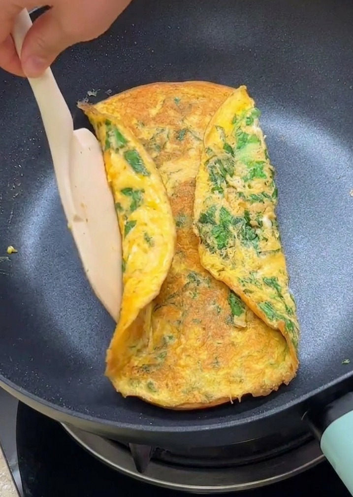 Una spatola che ripiega i bordi di unomelette alla lattuga sopra due metà di pane tostato in padella.