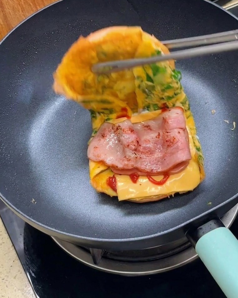 Pinze che piegano le due metà del burger avvolto nelluovo per formare un sandwich finito.