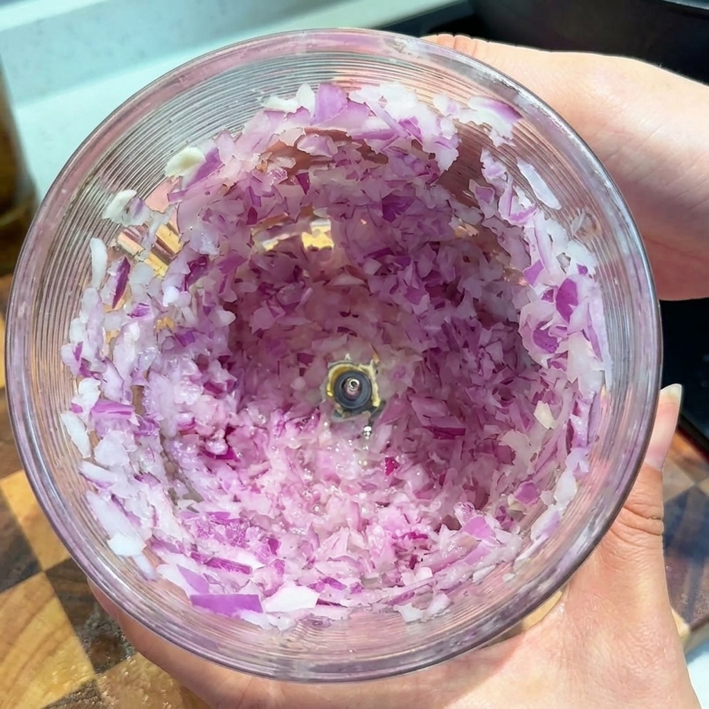 Pezzetti di cipolla rossa tritata finemente allinterno della ciotola di un robot da cucina trasparente.