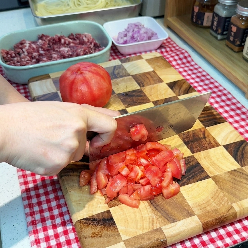 Una mano che usa un coltello largo per tagliare un pomodoro rosso pelato a piccoli cubetti su un tagliere.