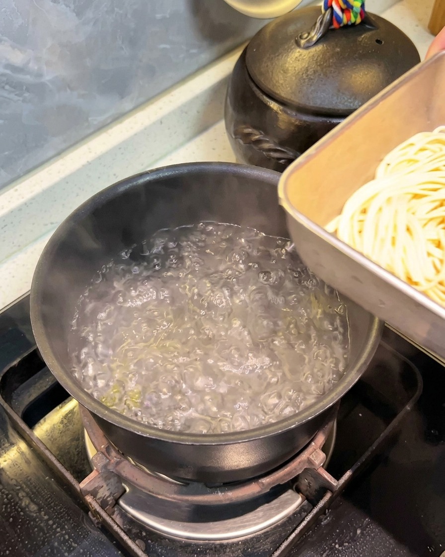 Spaghetti pre-idratati trasferiti da una teglia di metallo in una pentola di acqua bollente.