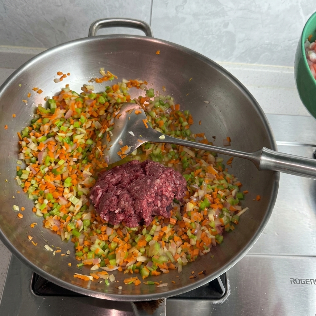 Macinato di maiale e manzo crudo sopra un letto di verdure soffritte in un wok dacciaio.