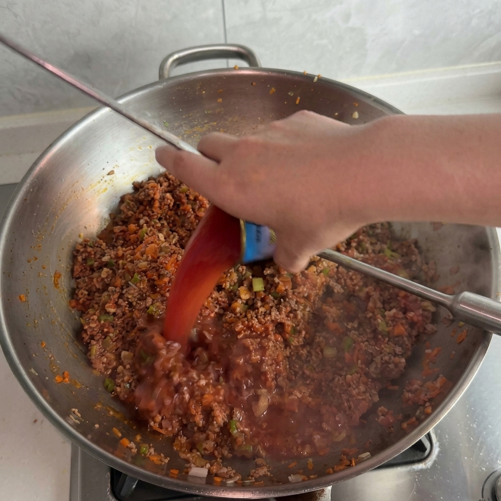 Acqua colorata dal residuo di pomodoro versata da un barattolino di latta nel sugo bollente.