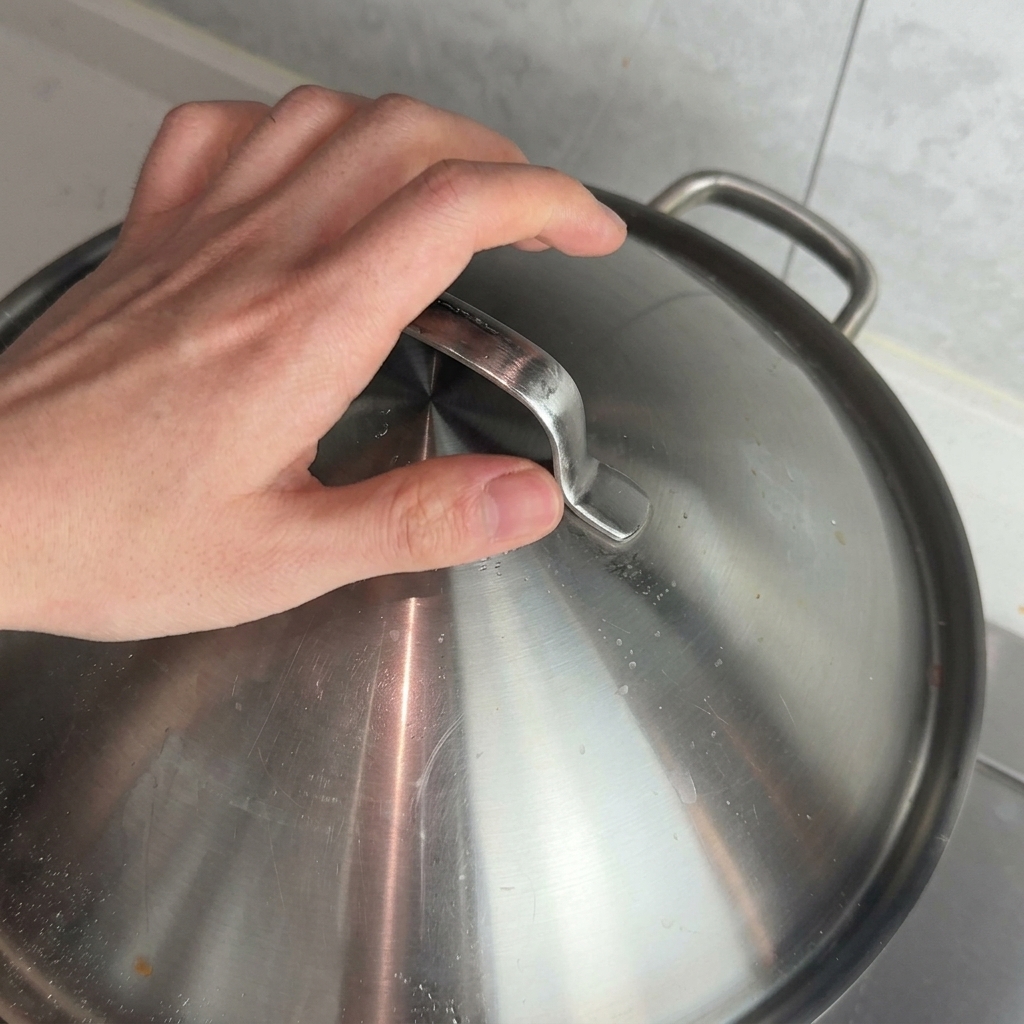 Una mano appoggia un coperchio di metallo su una pentola per far sobbollire il ragù.