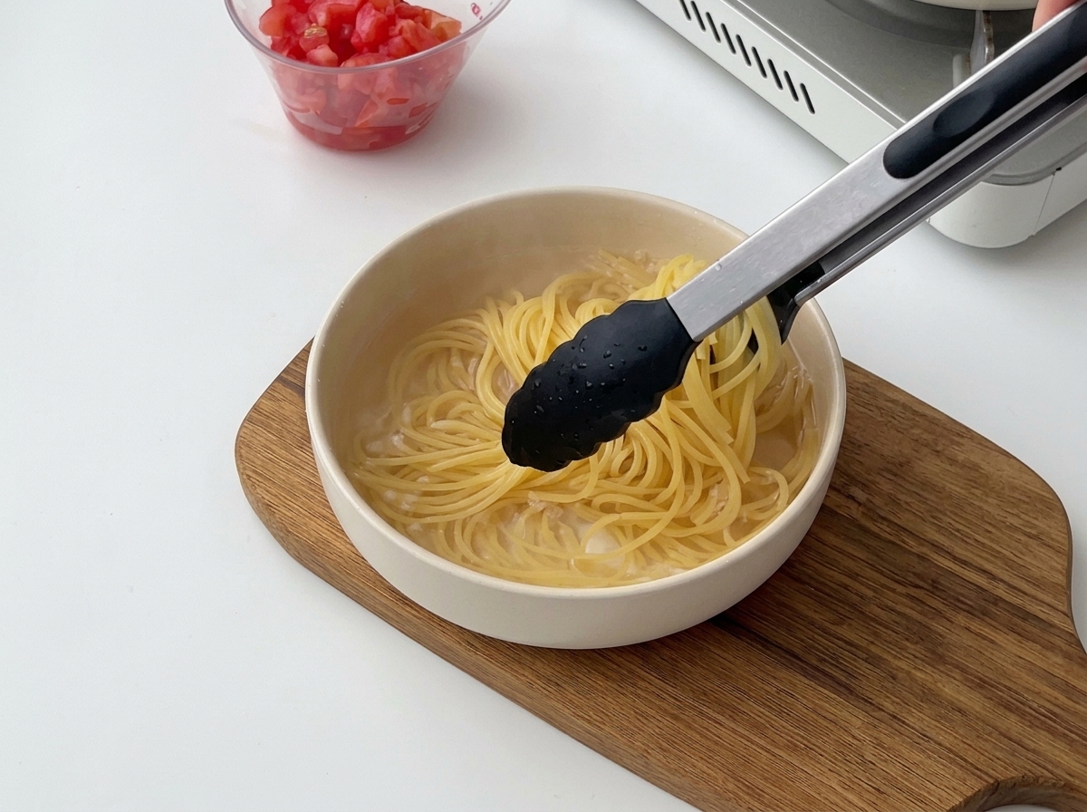 Pinze nere che sollevano spaghetti cotti dallacqua calda per trasferirli in una ciotola di acqua fredda.