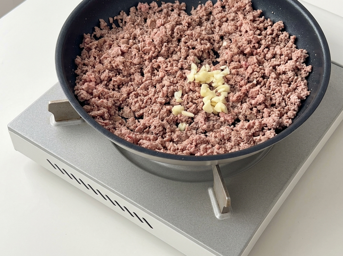 Aglio tritato posto sopra la carne macinata rosolata in una padella scura.