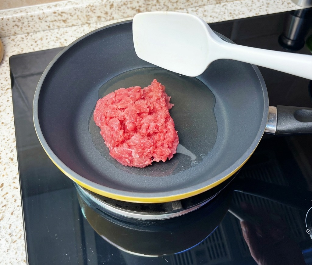 Carne di manzo macinata aggiunta in una padella calda con olio usando una spatola bianca.