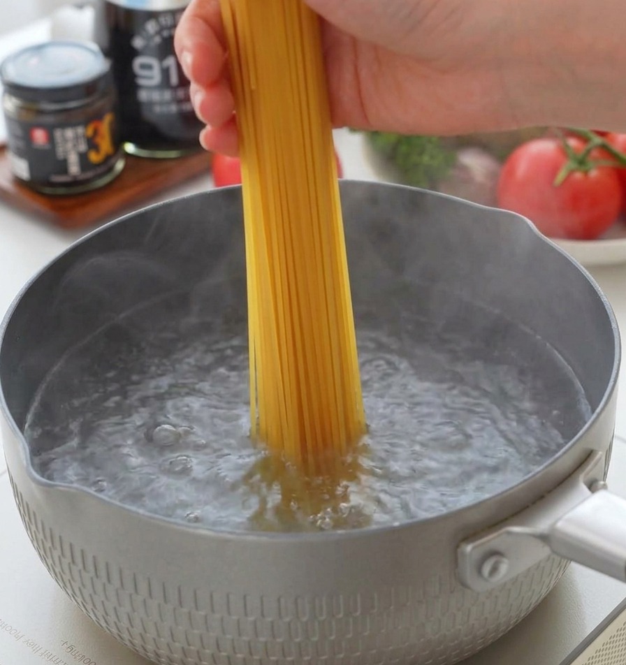 Spaghetti secchi inseriti verticalmente in una pentola di acqua bollente salata.