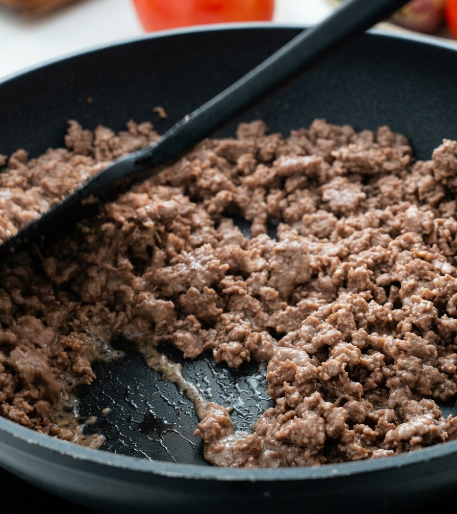 Carne macinata ben rosolata che salta in padella con una spatola.