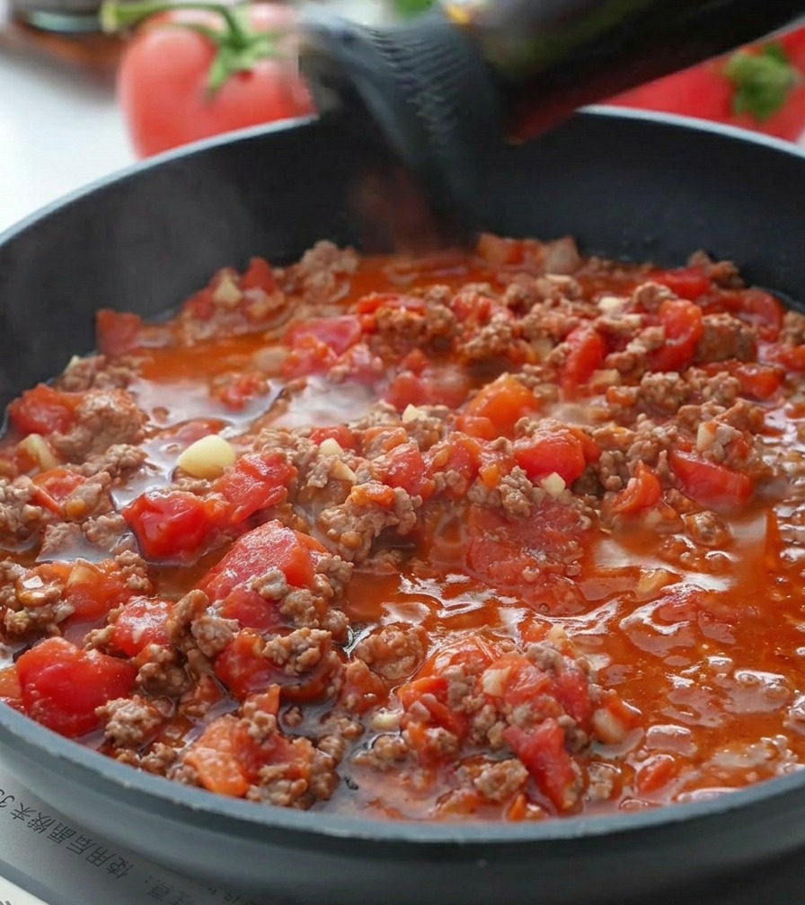 Salsa dostrica versata in un ragù di pomodoro e carne che sobbolle.