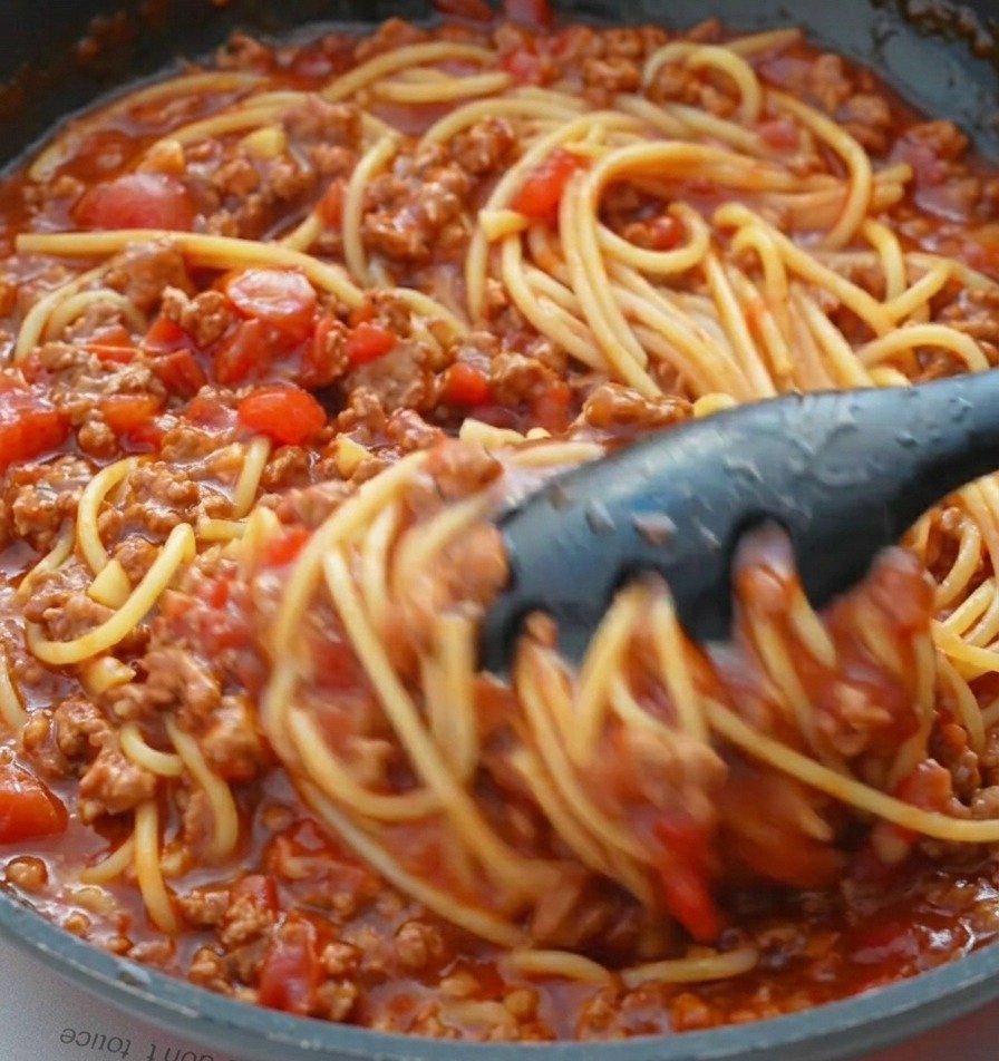 Pinze che saltano gli spaghetti nel ragù denso per condirli uniformemente.